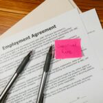 Top view of employment agreement contract with pens and seasonal hire note on wooden desk.